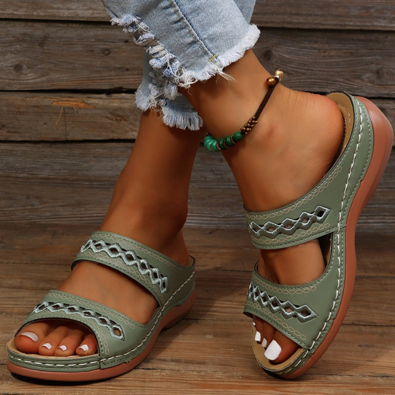 Sandales vertes en cuir pour femme avec motifs géométriques, portées avec un jean déchiré et un bracelet de cheville perlé. Mode estivale décontractée.