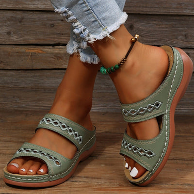 Sandales vertes en cuir pour femme avec motifs géométriques, portées avec un jean déchiré et un bracelet de cheville perlé. Mode estivale décontractée.