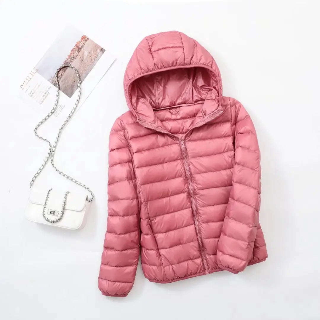 Veste matelassée rose avec capuche, posée à plat, accompagnée d'un sac à main blanc à chaîne argentée. Mode féminine, vêtements d'hiver.