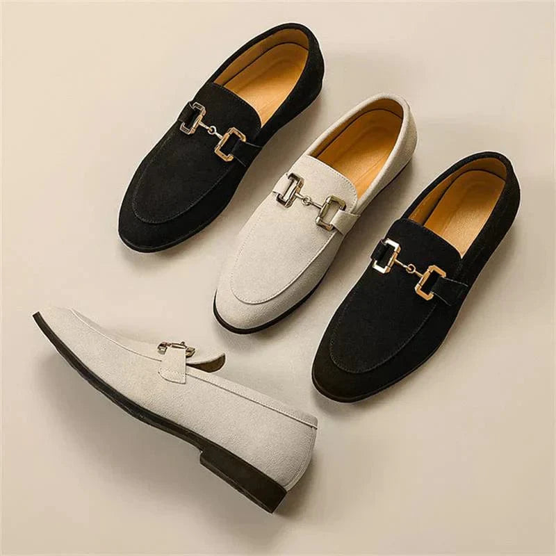 Quatre mocassins élégants en daim noir et beige avec boucles métalliques, posés sur une surface beige. Chaussures tendance pour hommes.