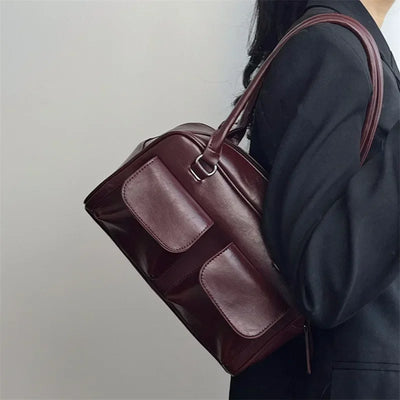 Sac à main en cuir marron porté par une femme en manteau noir, design élégant avec poches avant, accessoire de mode chic et tendance.