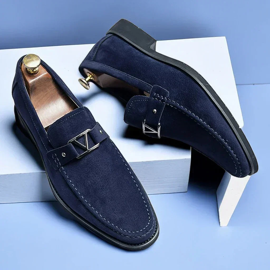 Mocassins en daim bleu marine élégants pour hommes avec boucle métallique, posés sur fond bleu. Chaussures de luxe, mode masculine, style raffiné.