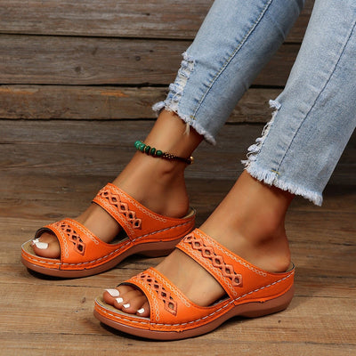 Sandales orange en cuir pour femme avec talons compensés, portées avec un jean déchiré. Chaussures d'été élégantes et confortables.