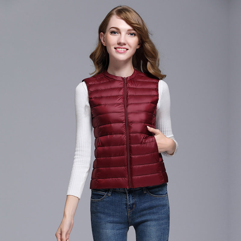 Femme portant une doudoune sans manches bordeaux, sur un pull blanc, avec un jean bleu. Mode automne, tenue décontractée, style moderne.