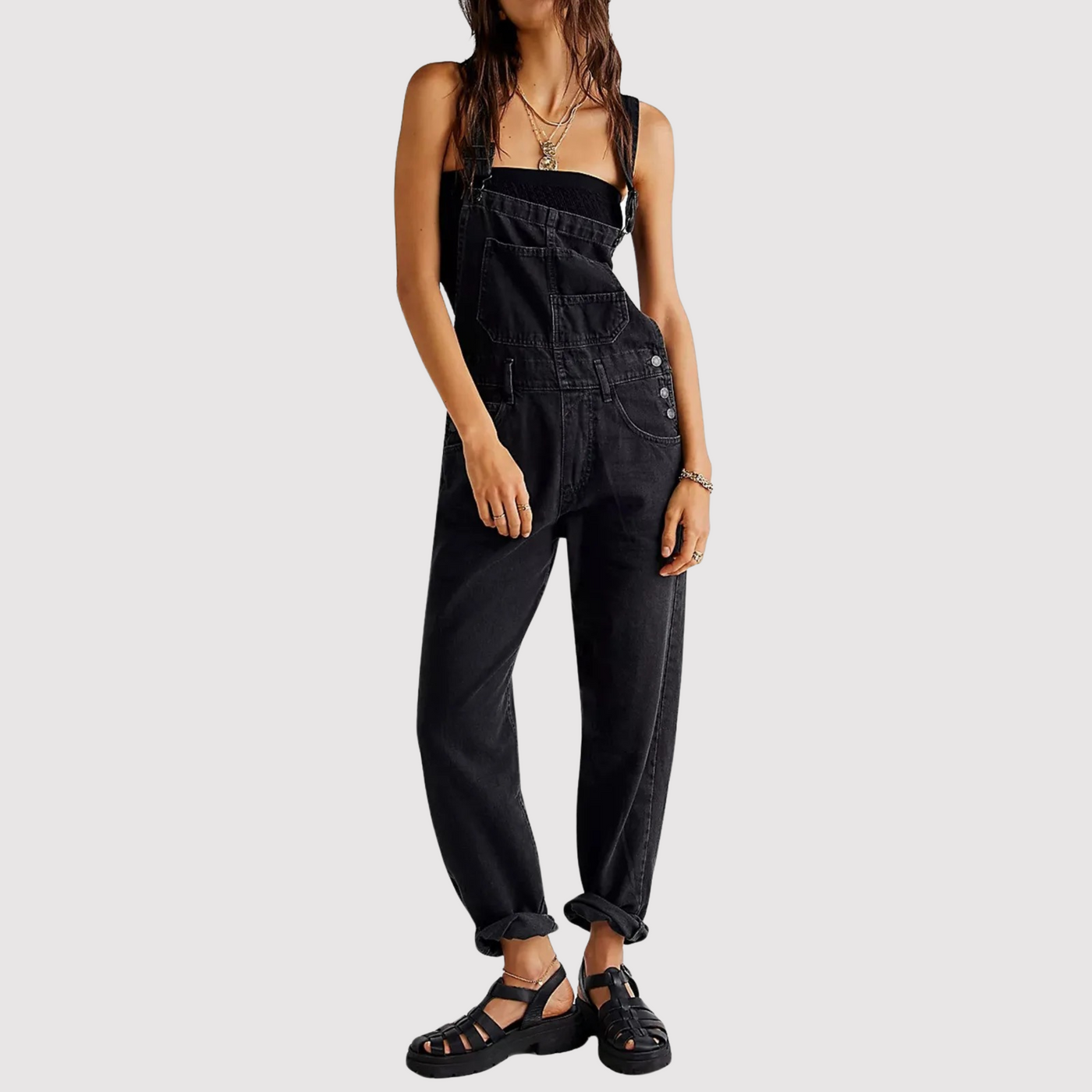 Femme portant une salopette noire en denim, style décontracté, avec des sandales noires. Mode tendance, tenue urbaine chic.