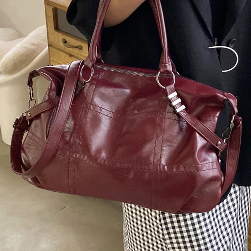Sac à main en cuir rouge bordeaux, élégant et spacieux, avec bandoulière réglable, porté par une personne en tenue chic. Accessoire mode tendance.