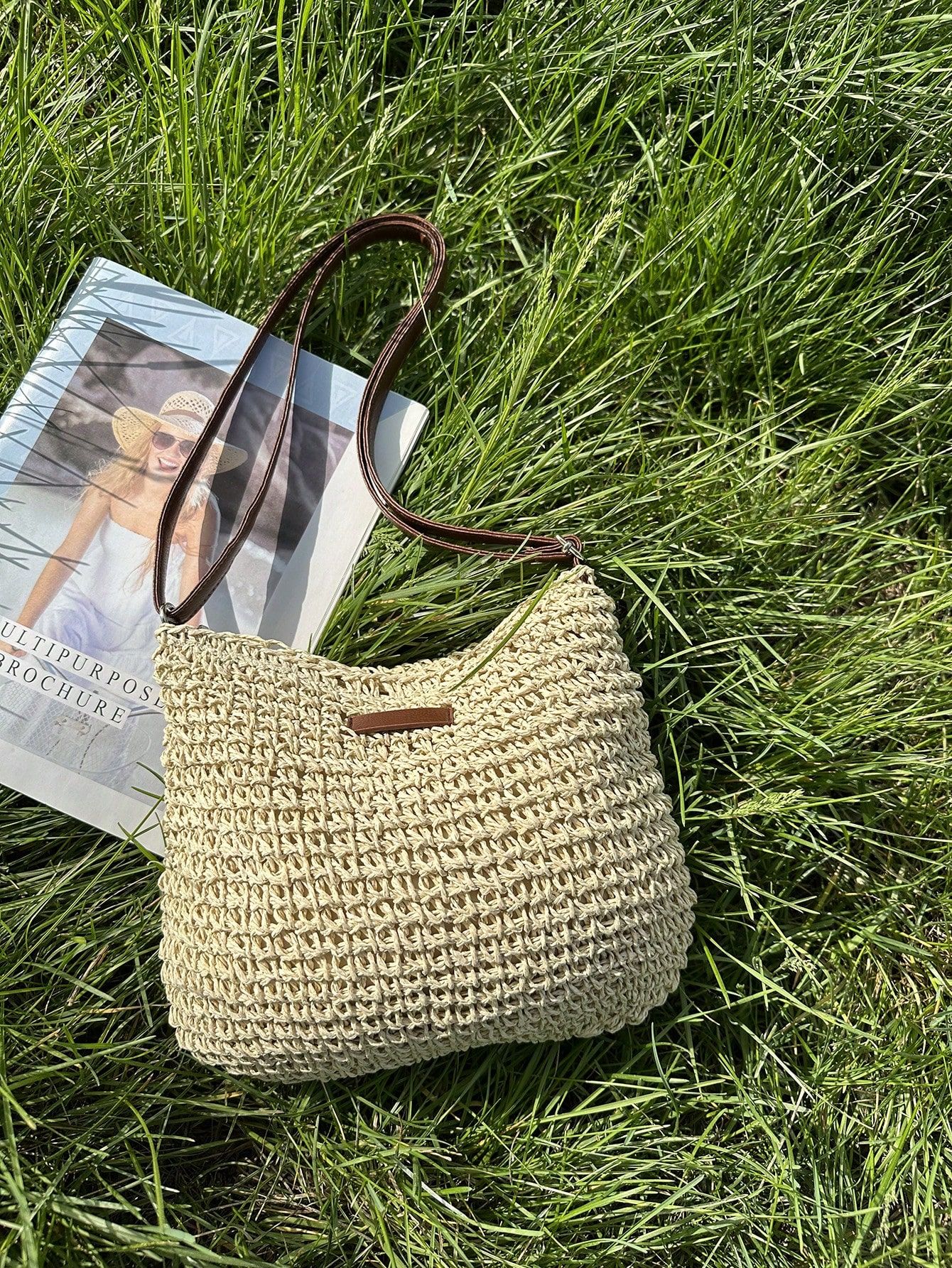 Sac en paille tressée beige sur herbe verte, à côté d'un magazine. Mode estivale, accessoire tendance, style décontracté.