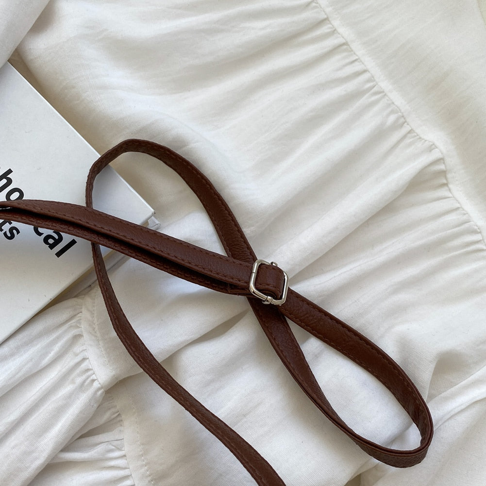 Ceinture en cuir marron posée sur une robe blanche plissée, avec un livre en arrière-plan. Accessoire de mode élégant et tendance.