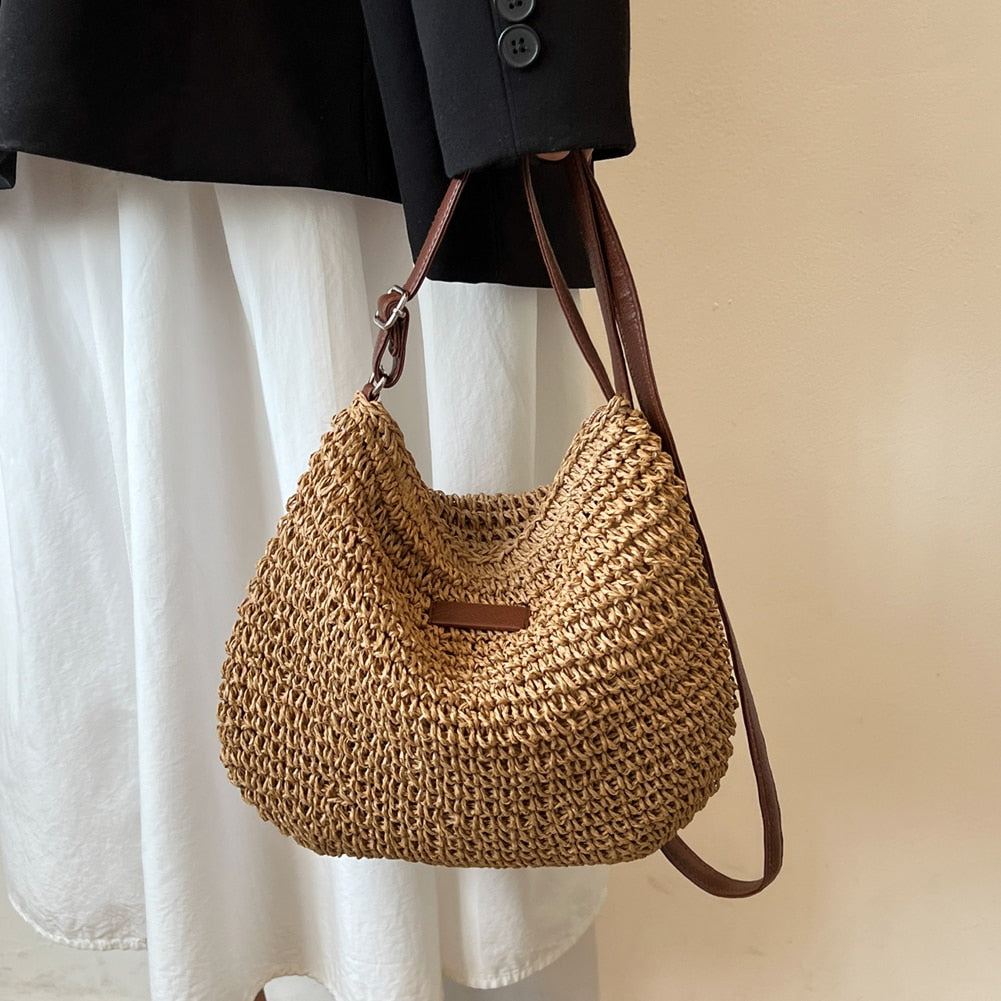 Sac à main en paille tressée avec bandoulière en cuir marron, porté sur une jupe blanche et veste noire. Accessoire mode tendance et estival.