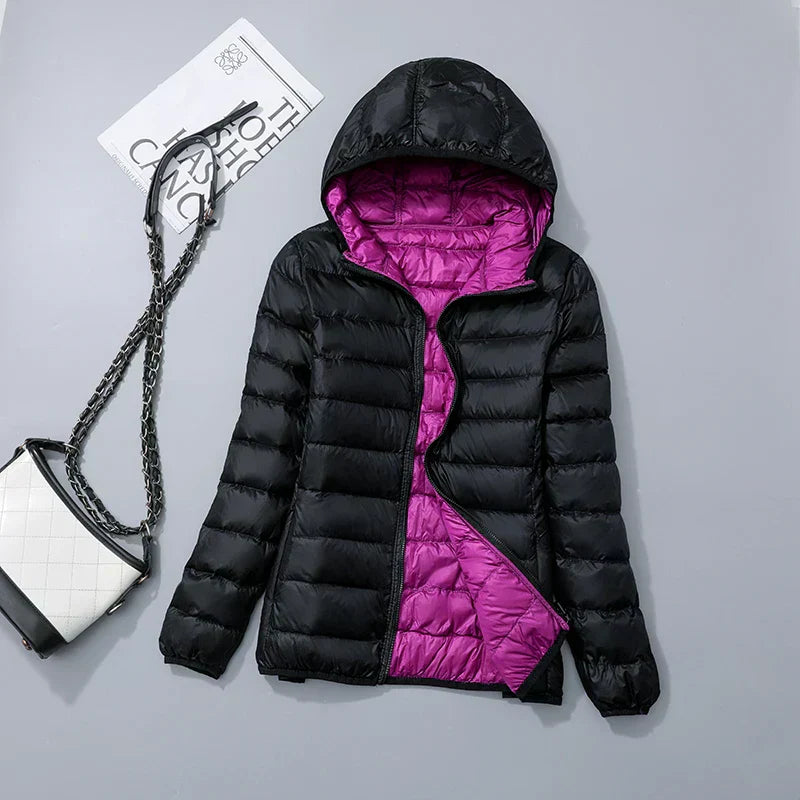 Veste doudoune noire avec doublure violette, capuche, posée à plat. Sac à main blanc et noir avec chaîne à côté. Mode hiver femme élégante.