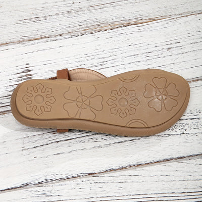 Sandale marron en cuir avec semelle en caoutchouc à motifs floraux, posée sur un sol en bois blanc. Chaussure d'été confortable et élégante.