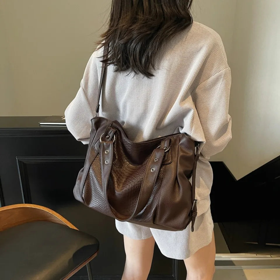 Femme portant un sac à main en cuir marron, tenue décontractée, intérieur moderne. Mode féminine, accessoire tendance, style élégant.