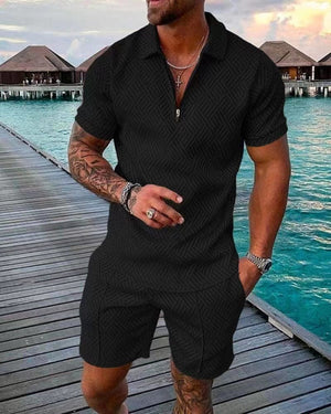 Homme en tenue noire élégante sur un ponton en bois, avec bungalows sur l'eau en arrière-plan, ciel partiellement nuageux. Mode masculine, vacances tropicales.