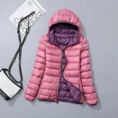 Doudoune rose à capuche avec doublure violette, posée sur fond gris, accompagnée d'un sac à main blanc et noir. Mode hiver femme tendance.