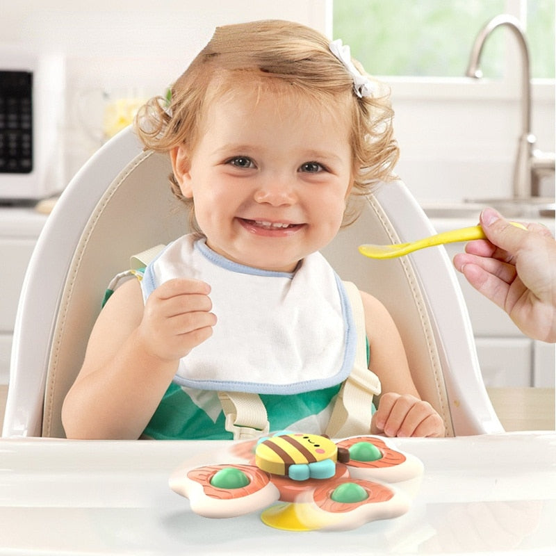 Jeune enfant souriant dans une chaise haute, tenant une cuillère jaune, avec un jouet abeille coloré sur la table. Repas bébé, cuisine lumineuse.