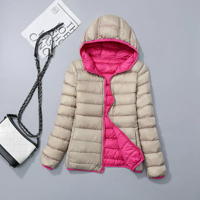 Veste matelassée réversible beige et rose avec capuche, posée à côté d'un sac à main noir et blanc et d'un magazine sur fond gris.