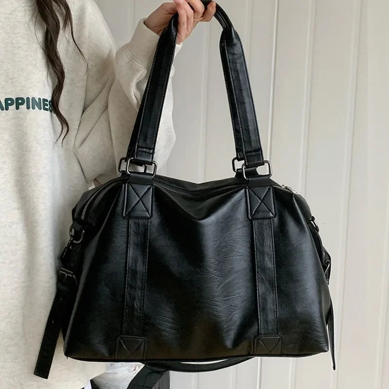 Sac à main noir en cuir porté par une personne en pull blanc. Design élégant avec doubles anses, idéal pour mode féminine et accessoires tendance.