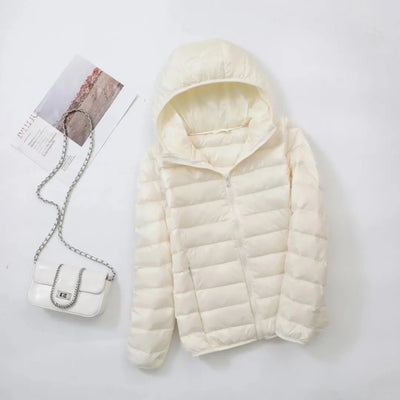 Veste matelassée blanche avec capuche sur fond blanc, accompagnée d'un sac à main blanc à chaîne argentée et magazine. Mode hiver élégante.