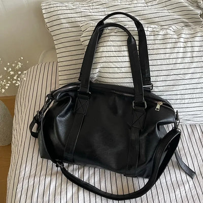 Sac à main en cuir noir élégant sur un lit à rayures, design moderne avec poignées robustes et bandoulière, accessoire mode tendance.