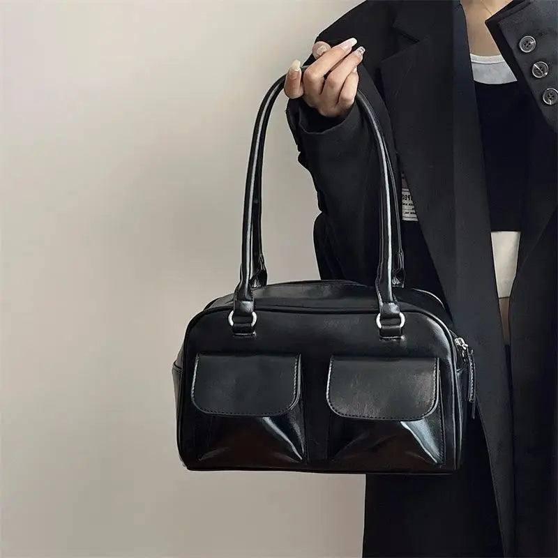 Sac à main noir élégant en cuir avec deux poches avant, porté par une personne en manteau noir. Accessoire mode chic et tendance.