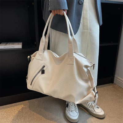 Sac à main blanc élégant en cuir avec poche zippée, porté par une personne en pantalon beige et baskets blanches. Mode, accessoires, tendance.