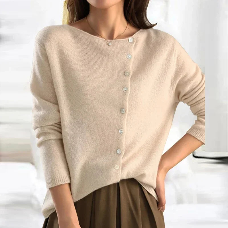 Femme portant un pull beige en cachemire avec boutons asymétriques, manches longues, col bateau, style élégant et décontracté. Mode automne-hiver.