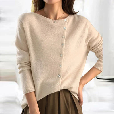Femme portant un pull beige en cachemire avec boutons asymétriques, manches longues, col bateau, style élégant et décontracté. Mode automne-hiver.