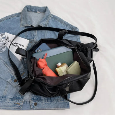 Sac à main noir ouvert sur veste en jean, contenant un parapluie rouge, un smartphone, une tablette, un livre, un portefeuille et une bouteille.
