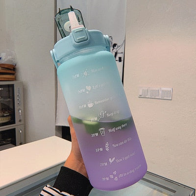Bouteille d'eau dégradée bleu-violet avec marqueurs horaires et messages motivants, couvercle à paille, tenue par une main. Hydratation, fitness.