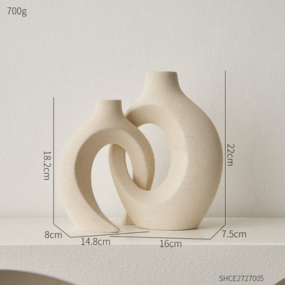 Deux vases décoratifs en céramique beige, design moderne et sculptural, dimensions indiquées, posés sur une étagère blanche.
