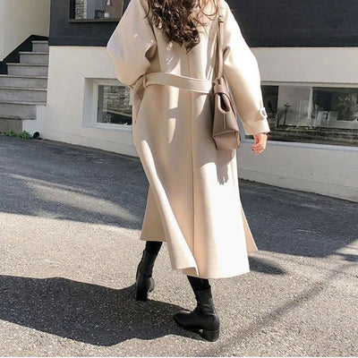 Femme portant un manteau beige élégant, sac à main marron, bottes noires, marchant en ville. Mode automne, style urbain chic, tendance 2023.