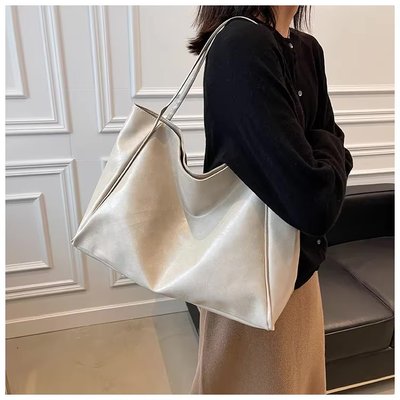 Femme portant un grand sac à main en cuir blanc, tenue élégante avec pull noir et jupe beige, intérieur moderne. Accessoire mode chic.