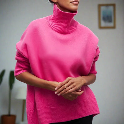 Femme portant un pull rose vif à col roulé, manches retroussées, dans un intérieur moderne. Mode automne, style décontracté, tendance féminine.