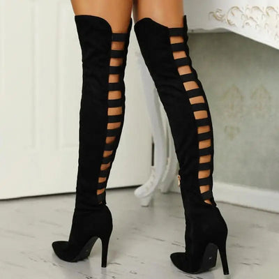 Cuissardes noires à talons hauts avec découpes latérales, posées sur un sol en bois clair, devant une porte blanche. Mode féminine élégante.