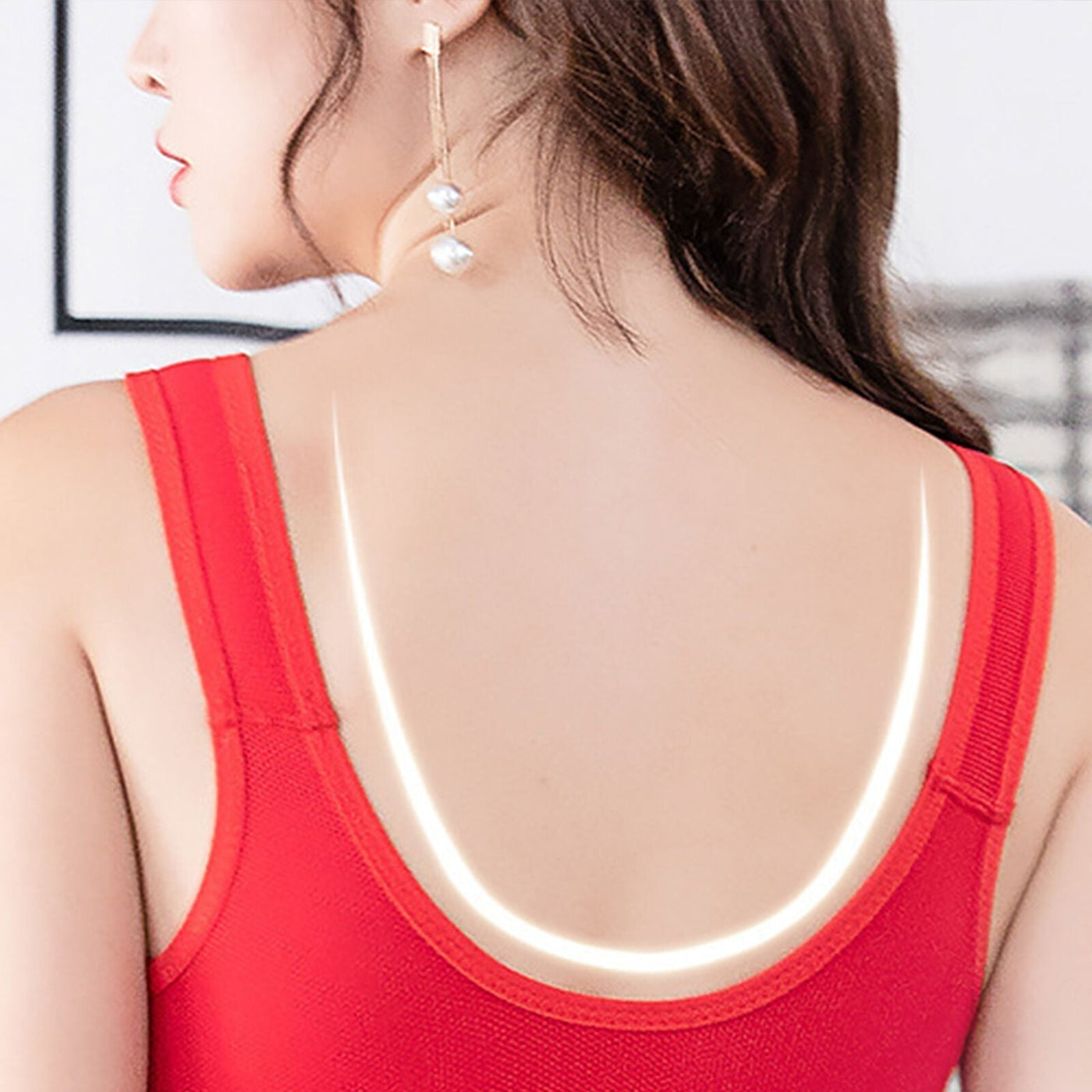Femme de dos portant un débardeur rouge avec bretelles lumineuses, cheveux bruns ondulés, boucle d'oreille pendante, style moderne et élégant.