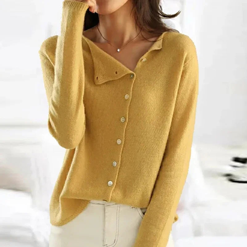 Femme portant un pull jaune en laine avec boutons, style décontracté, manches longues, col asymétrique, mode automne-hiver, intérieur lumineux.