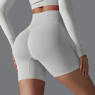 Dame en tenue de sport blanche moulante, vue de dos, mettant en valeur des shorts de fitness taille haute. Mode active, vêtements de sport élégants.