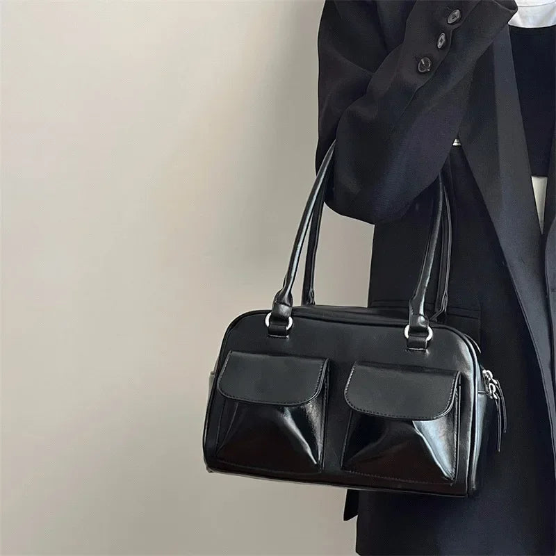 Sac à main noir élégant en cuir avec deux poches avant, porté par une personne en manteau noir. Accessoire mode chic et tendance.
