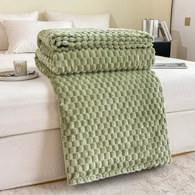 Couverture en peluche verte texturée sur un lit blanc, avec oreillers blancs et une tasse sur la table de chevet. Décoration chambre moderne et cosy.