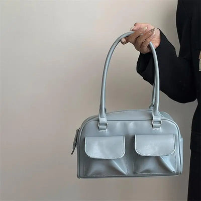 Sac à main bleu clair élégant avec deux poches avant, porté par une personne en veste noire. Accessoire mode tendance pour femmes.
