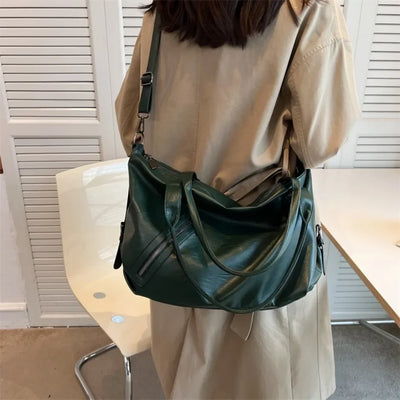 Sac à main vert en cuir porté par une femme en manteau beige, devant une chaise blanche. Mode féminine, accessoire tendance, style élégant.