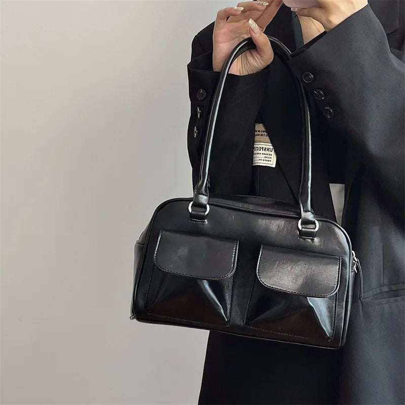 Sac à main en cuir noir élégant avec deux poches avant, porté par une personne en manteau noir. Accessoire mode chic et tendance pour femmes.