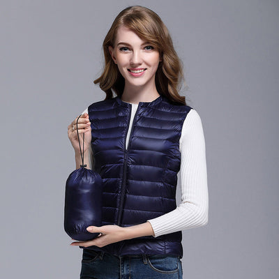 Femme souriante portant une doudoune sans manches bleu marine, tenant un sac de rangement assorti. Mode automne, vêtements légers, style décontracté.