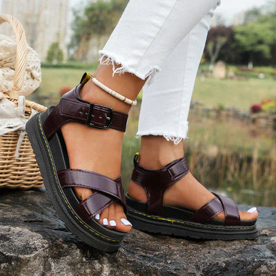 Sandales marron en cuir pour femme avec semelle épaisse, portées avec un jean blanc déchiré. Mode estivale, chaussures confortables, tendance.