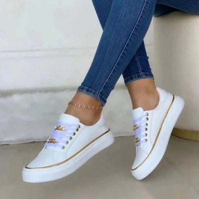 Chaussures blanches élégantes avec détails dorés, portées avec un jean slim. Sneakers tendance pour un look décontracté et moderne.