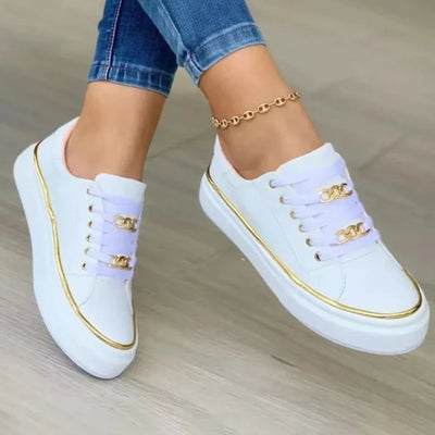 Chaussures blanches décontractées pour femme avec détails dorés, portées avec un jean. Sneakers tendance, mode féminine, style urbain.