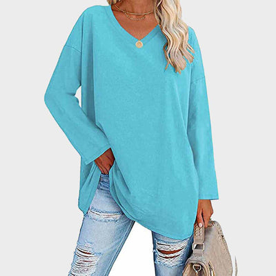 Femme portant un pull bleu ample à col en V, associé à un jean déchiré et un sac beige. Mode décontractée, tendance automne-hiver.