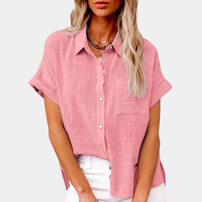 Chemisier rose en lin pour femme, manches courtes, col classique, boutons blancs, porté avec un pantalon blanc. Mode féminine élégante et décontractée.