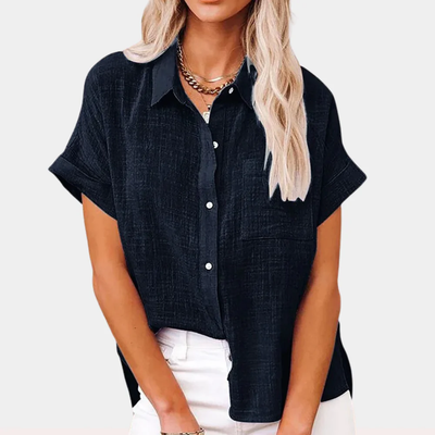 Blouse noire en lin pour femme, manches courtes, col chemise, boutons blancs, portée avec un pantalon blanc. Mode féminine élégante et décontractée.