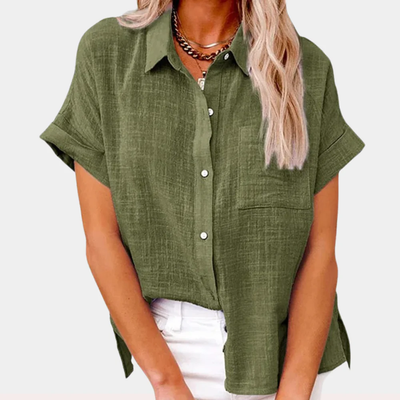 Chemisier vert en lin pour femme avec manches courtes, col classique et poche poitrine, porté avec un pantalon blanc. Mode féminine élégante.